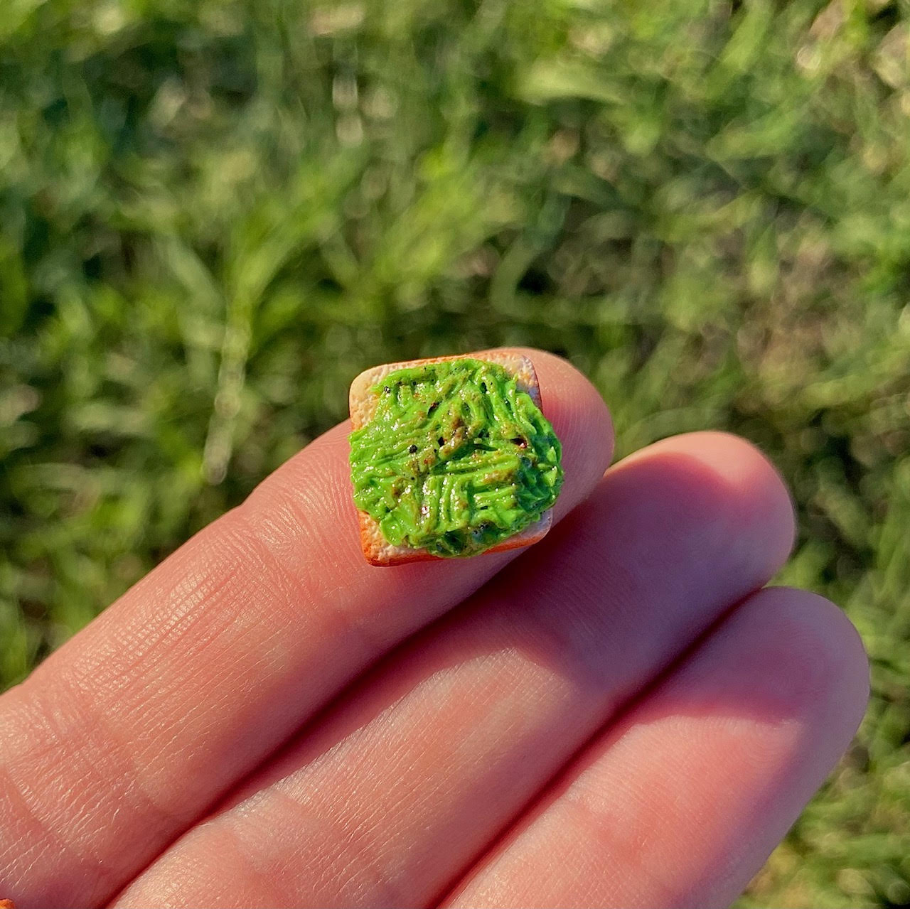 1/2 in by 1/2 in dollhouse size slice of miniature toast with glossy mashed avocado + seasonings spread across the entire top of the bread.